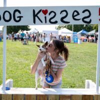 woman kissing her small dog at Dog Kisses booth at Royal Oak's Barktoberfest