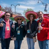 4 friends smiling at camera wearing sombreros and cheering with beer cans