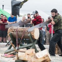 two men in flannel shirts sawing a log while onlookers watch during Wyandotte's Fire & Flannel Festival
