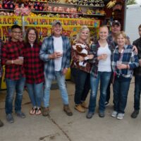 group of friends in flannel shirts with beer cups in hand standing in front of carnival game during Wyandotte's Fire & Flannel Festival