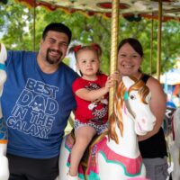 mom, dad, and little girl smiling at camera on carousel at carnival rides and US Army Nike Missile monument at Riverview Summerfest