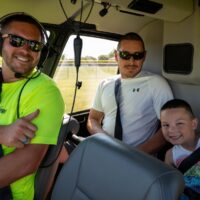 pilot, father, and young sun smiling at the camera while sitting in a helicopter at Riverview Summerfest