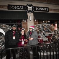 three friends standing in front of tent igloos on patio of Bobcat Bonnie's during Wyandotte's Santa Pub Crawl