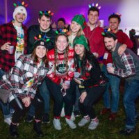 group of friends with ugly Christmas sweaters and Christmas light headbands in white tent at Wyandotte's Santa Pub Crawl