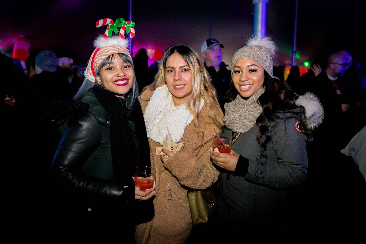 three friends holding cocktail glasses; one wearing a fun candy cane headband, at Wyandotte's Winter Beer Cocktail Fest