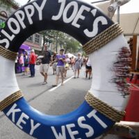 Inner-tube sign saying Sloppy Joe's Key West with crowd walking by at vendor booth during Wyandotte's Street Art Fair