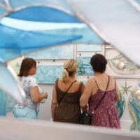 three woman looking at ocean related art and stained glass in vendor booth at Wyandotte's Street Art Fair