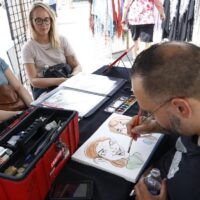 artist painting caricatures of two young girls in booth at Wyandotte's Street Art Fair