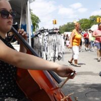 musician playing violin in front of sheet music while crowd walks by at Wyandotte's Street Art Fair