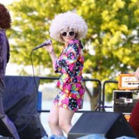 three band members in afro wigs on stage at Wyandotte's Street Art Fair