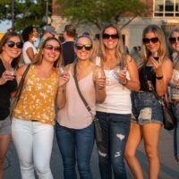 group of ladies in sunglasses with wine glasses posing for camera during Wyandotte's Wine Crawl