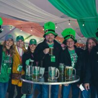 group of party goers in green leprechaun hats and gear in front of table full of green beer