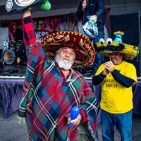 man wearing sombrero and poncho holding up a Tacos, Hops, & Tequila Sombrero Contest champion wrestlers-style belt