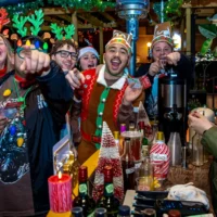 Happy group in Christmas sweaters and fun Christmas outfits at a bar station serving drinks.